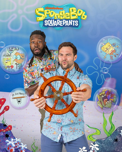 two-men-standing-with-a-steering-wheel-against-a-spongebob-squarepants-themed-background-wearing-rsvlts-spongebob-kunuflex-shirts