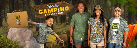 four-people-posing-in-matching-peanuts-camping-collection-outfits-against-a-forest-backdrop-with-a-hanging-sign-shows-peanuts-camping-collection-the-set-includes-a-child-holding-a-cardboard-suitcase-bundle-box-wearing-button-kids-polo-adults-wearing-rsvltsxpeanuts-patterned-shirts-tee-hats-and-a-visible-orange-tent-on-the-right